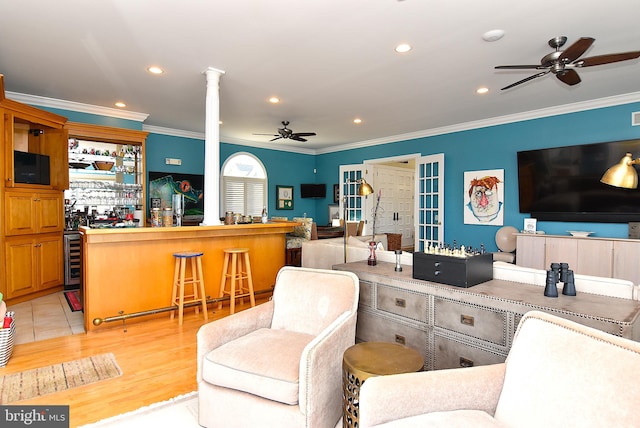 living room with ceiling fan, crown molding, beverage cooler, and ornate columns