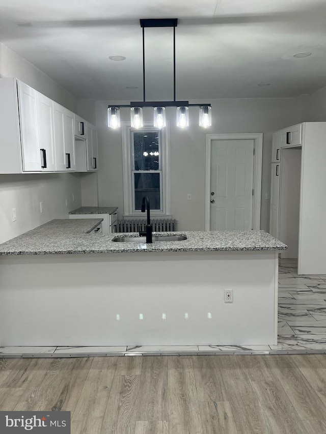 kitchen with light hardwood / wood-style flooring, kitchen peninsula, light stone counters, decorative light fixtures, and sink