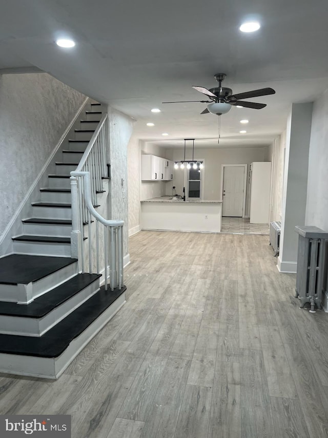 unfurnished living room with ceiling fan, light hardwood / wood-style floors, and radiator heating unit