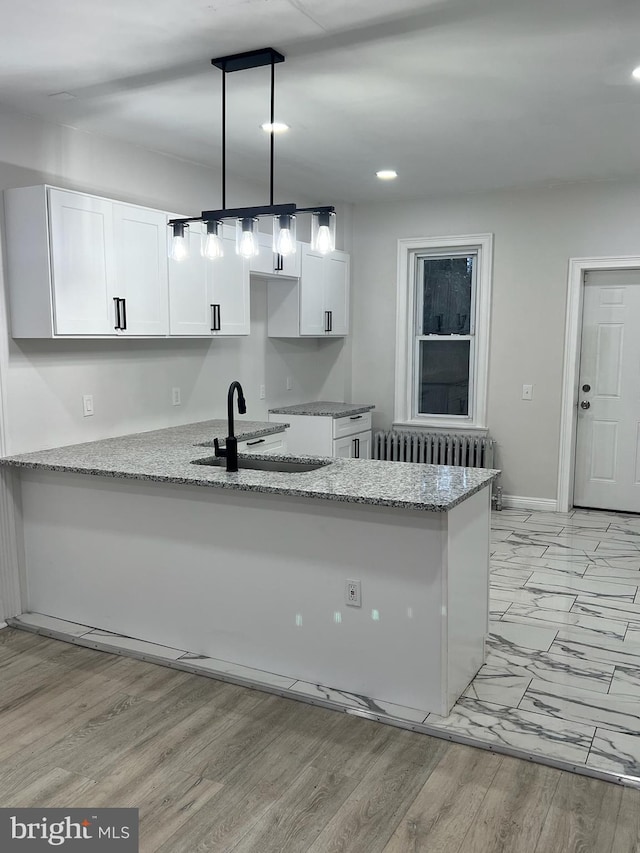 kitchen featuring sink, kitchen peninsula, light stone counters, and pendant lighting