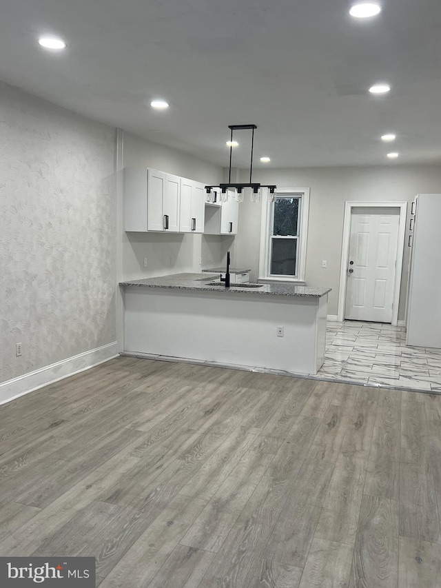 kitchen featuring hanging light fixtures, light hardwood / wood-style floors, kitchen peninsula, and white cabinetry