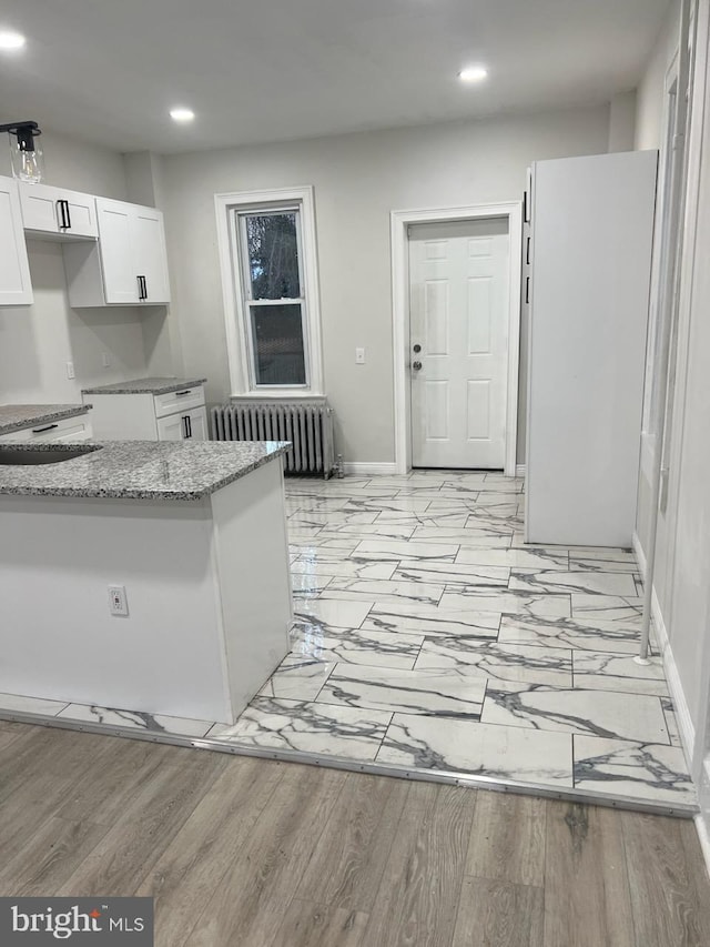 kitchen featuring white cabinetry, light hardwood / wood-style flooring, kitchen peninsula, light stone counters, and radiator heating unit