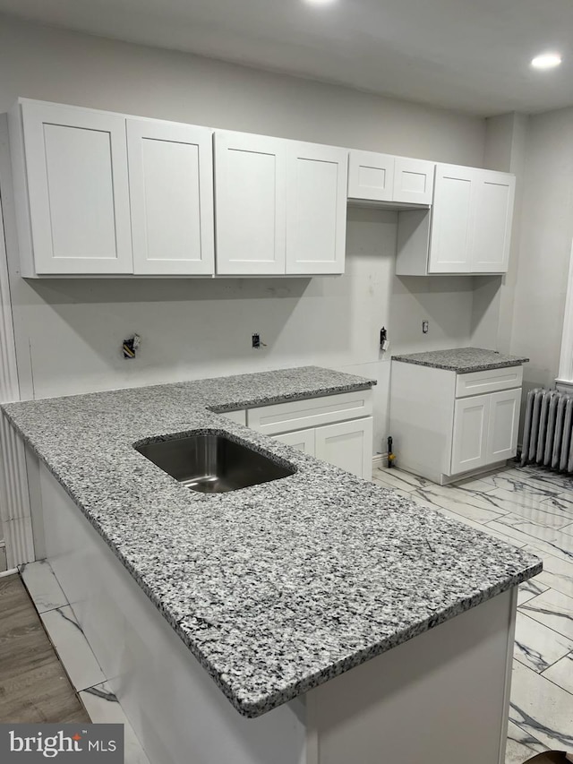 kitchen with white cabinetry, light stone countertops, light wood-type flooring, and radiator heating unit