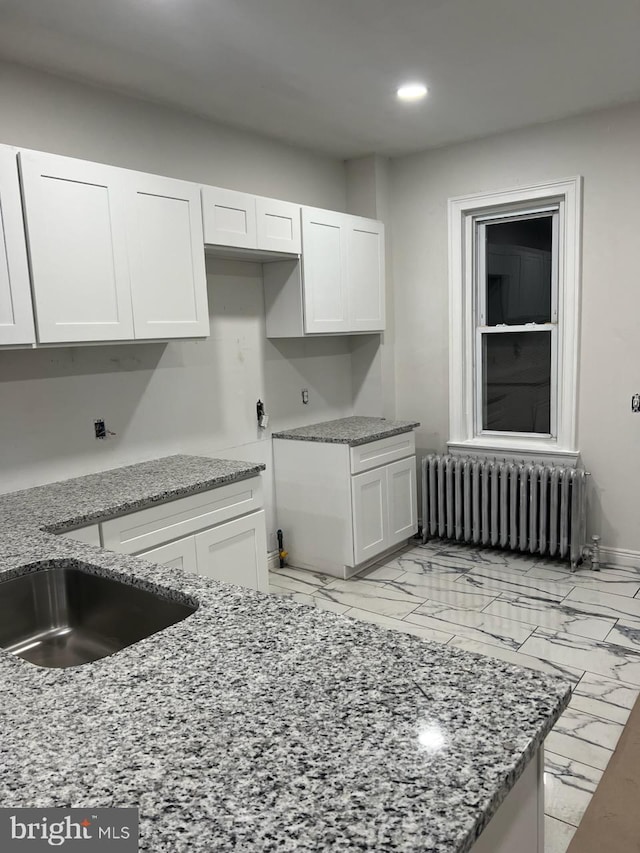 kitchen with light stone countertops, white cabinetry, light tile flooring, and radiator heating unit