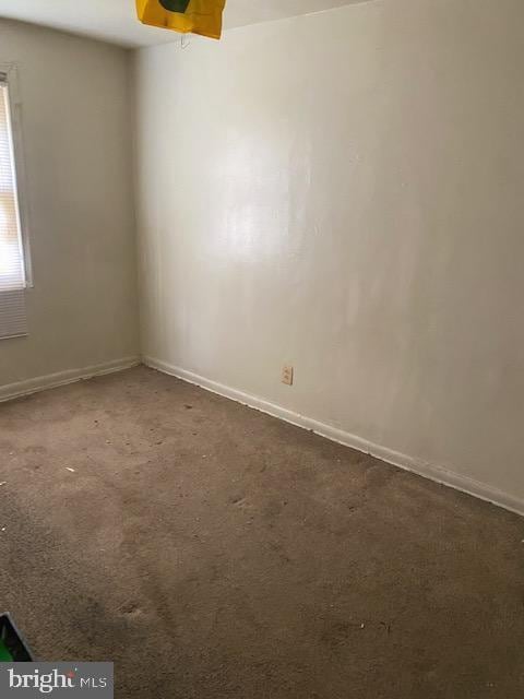 unfurnished room featuring dark carpet and baseboards