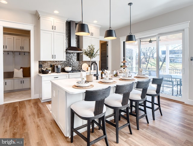 kitchen featuring pendant lighting, wall chimney exhaust hood, light hardwood / wood-style floors, and white cabinets