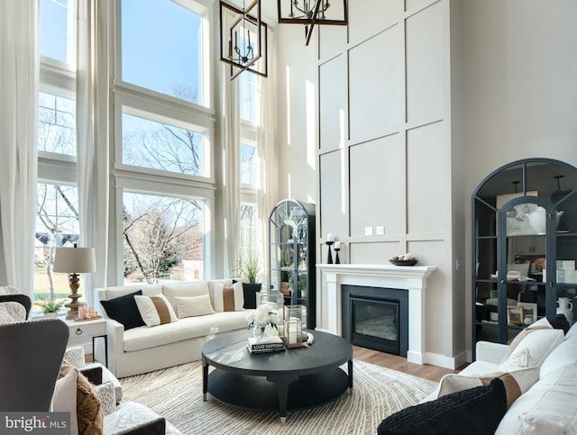 living room with a towering ceiling, an inviting chandelier, light hardwood / wood-style flooring, and a healthy amount of sunlight