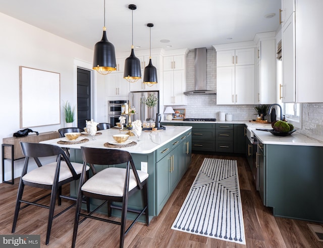 kitchen with wall chimney range hood, dark wood-type flooring, a center island, decorative light fixtures, and white cabinets