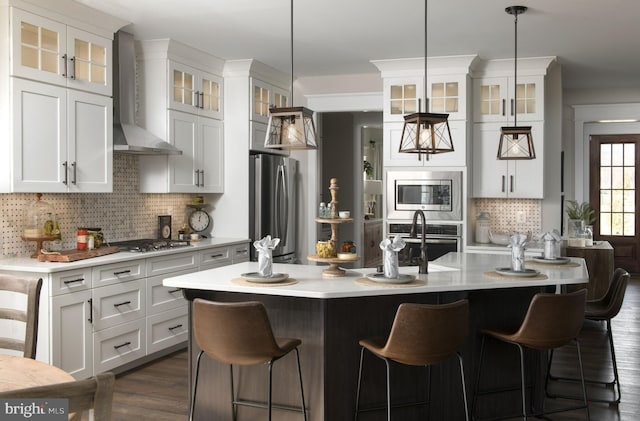 kitchen featuring decorative light fixtures, white cabinetry, decorative backsplash, stainless steel appliances, and wall chimney range hood