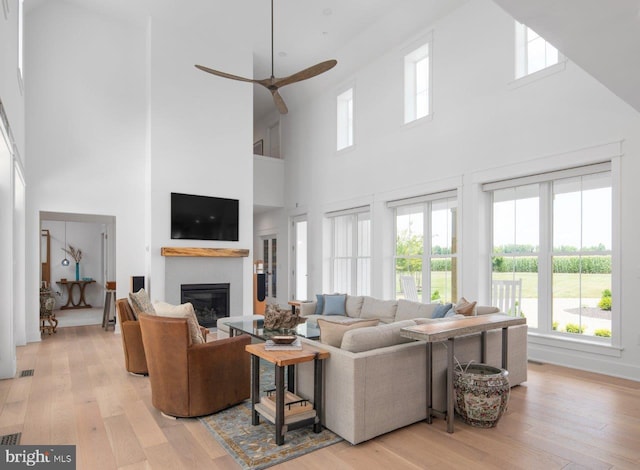 living room with ceiling fan, light hardwood / wood-style flooring, and a high ceiling