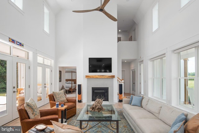 living room with a towering ceiling, ceiling fan, light hardwood / wood-style floors, and french doors