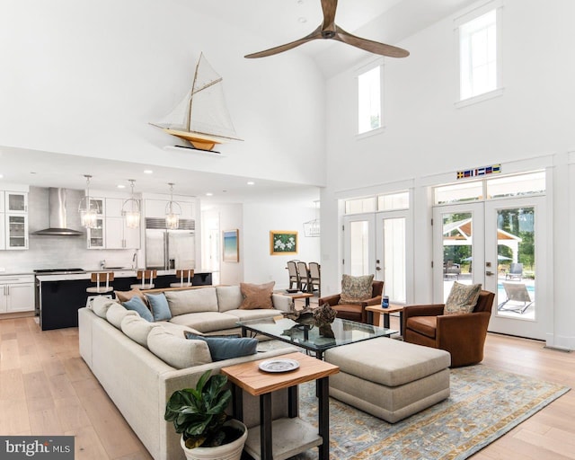 living room with a high ceiling, ceiling fan, light wood-type flooring, and french doors