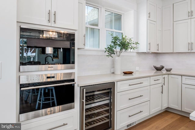 kitchen featuring tasteful backsplash, light hardwood / wood-style floors, beverage cooler, double oven, and white cabinetry