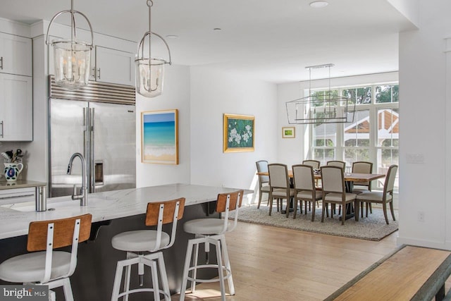 kitchen featuring light wood-type flooring, built in refrigerator, a chandelier, light stone countertops, and white cabinets