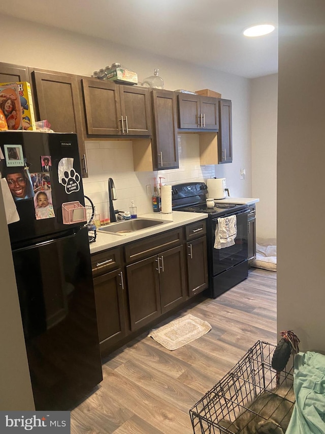 kitchen featuring sink, backsplash, black appliances, dark brown cabinetry, and light wood-type flooring