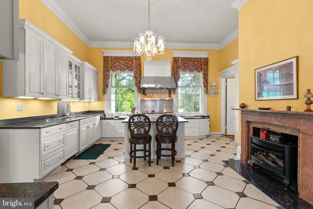 kitchen featuring a chandelier, light tile flooring, a kitchen bar, wall chimney exhaust hood, and white cabinets