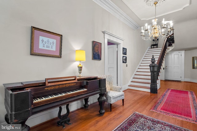 miscellaneous room with a tray ceiling, a notable chandelier, ornamental molding, and light hardwood / wood-style floors