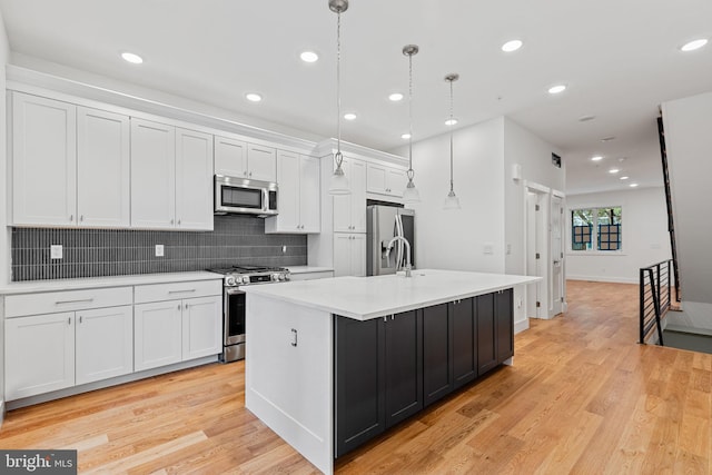 kitchen with hanging light fixtures, an island with sink, appliances with stainless steel finishes, white cabinetry, and light hardwood / wood-style flooring