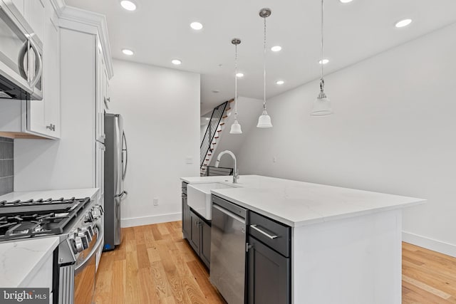 kitchen featuring appliances with stainless steel finishes, white cabinetry, a kitchen island with sink, and decorative light fixtures