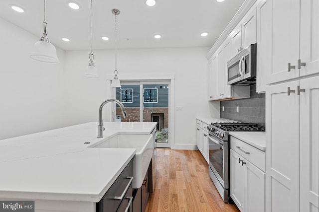 kitchen with appliances with stainless steel finishes, light hardwood / wood-style floors, decorative light fixtures, white cabinets, and a center island with sink