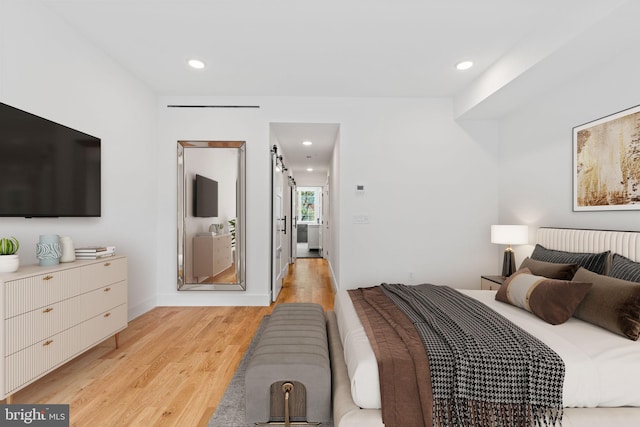 bedroom with a barn door and light wood-type flooring