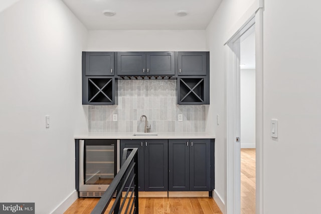 bar featuring sink, tasteful backsplash, light wood-type flooring, and beverage cooler