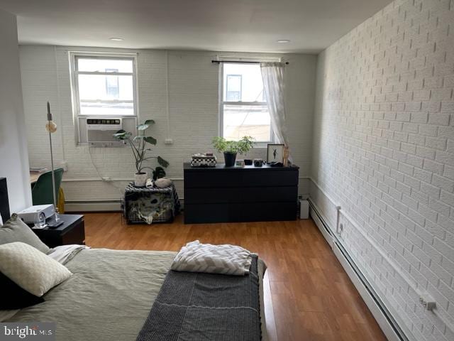 bedroom featuring brick wall, light hardwood / wood-style floors, and a baseboard radiator