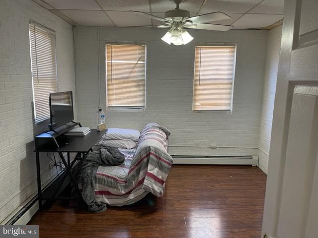 interior space featuring multiple windows, a baseboard radiator, dark wood-type flooring, and a drop ceiling