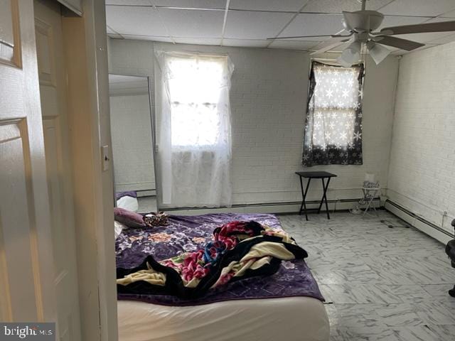 bedroom with ceiling fan, a drop ceiling, brick wall, and light tile floors