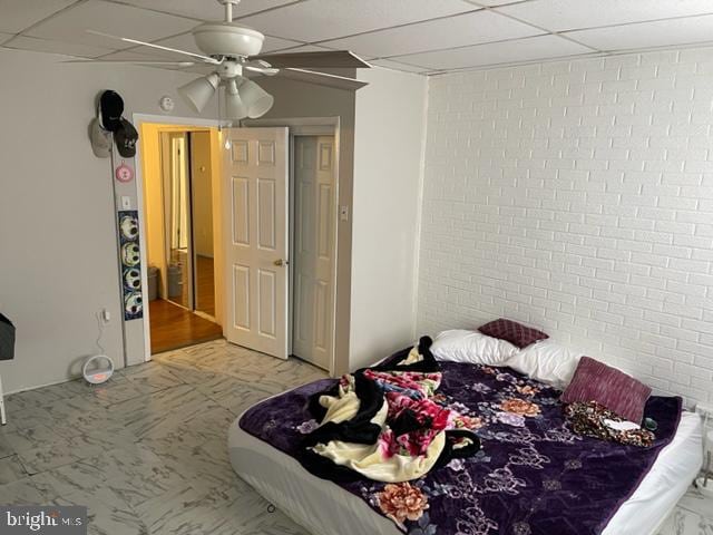 bedroom with brick wall, ceiling fan, and a drop ceiling