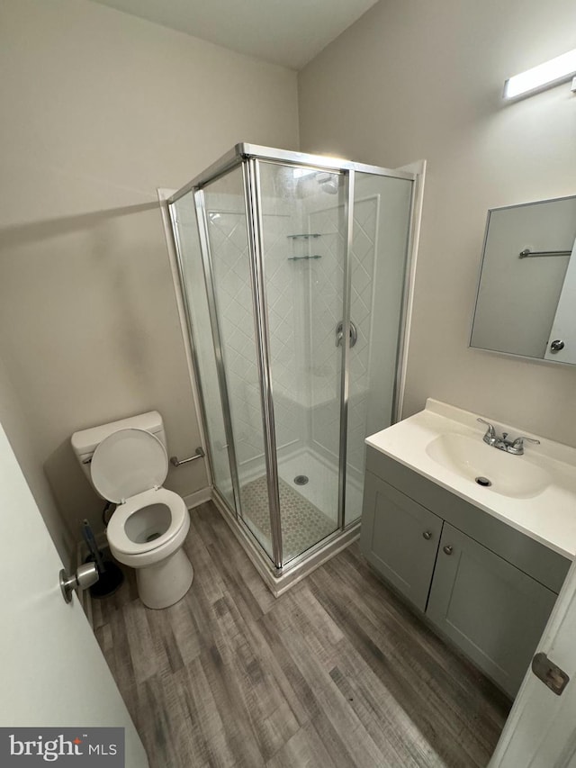 bathroom with a shower with shower door, wood-type flooring, vanity, and toilet