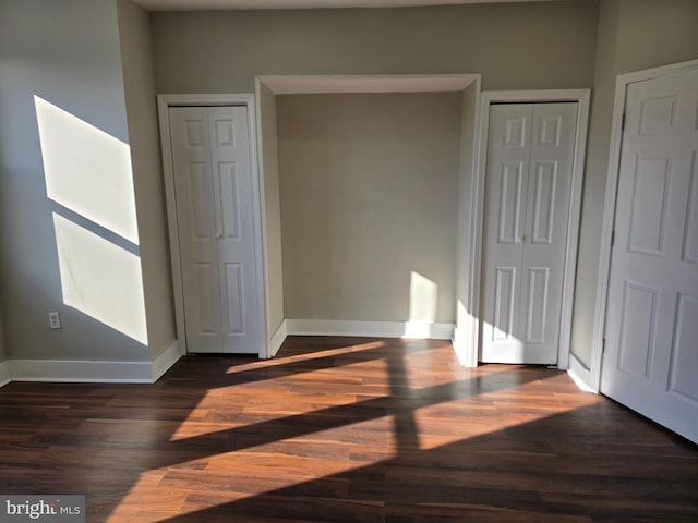 unfurnished bedroom featuring dark hardwood / wood-style flooring and multiple closets