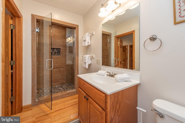 bathroom featuring toilet, a shower with shower door, wood-type flooring, vanity, and a textured ceiling