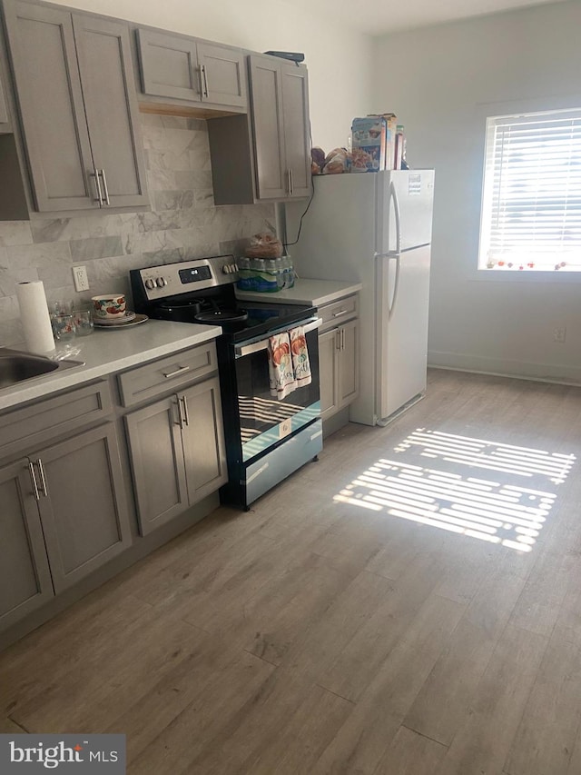 kitchen featuring stainless steel range with electric stovetop, light hardwood / wood-style flooring, gray cabinets, backsplash, and white fridge