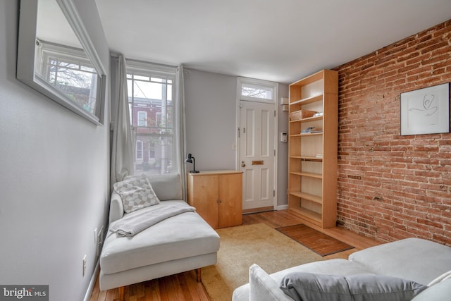 living area with wood-type flooring and brick wall