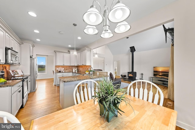 dining space featuring a chandelier, light hardwood / wood-style floors, a wood stove, sink, and vaulted ceiling