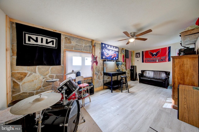 living room featuring light hardwood / wood-style flooring, ceiling fan, and a textured ceiling