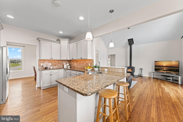 kitchen featuring light hardwood / wood-style flooring, white cabinetry, hanging light fixtures, a wood stove, and sink