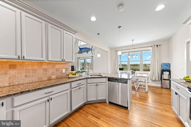 kitchen with decorative light fixtures, dishwasher, dark stone countertops, and light hardwood / wood-style floors