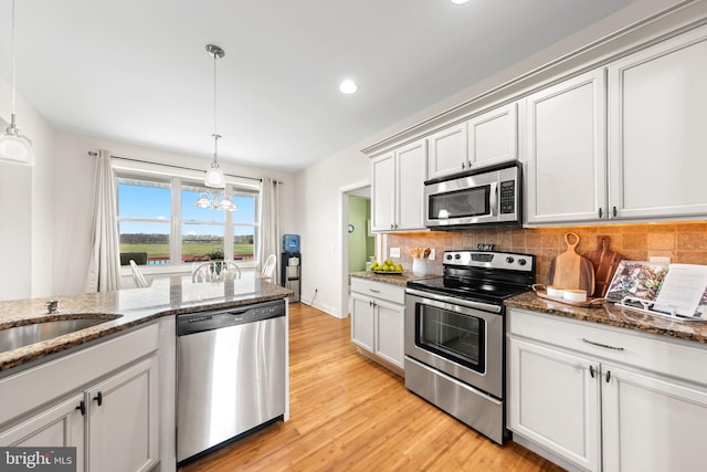 kitchen featuring stainless steel appliances, stone counters, light hardwood / wood-style flooring, hanging light fixtures, and an inviting chandelier