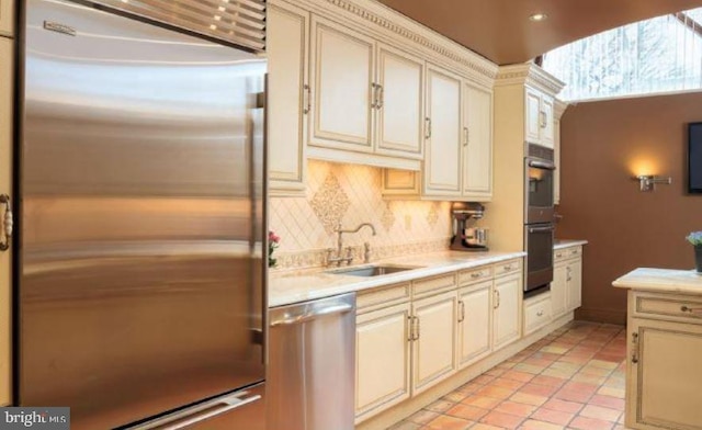 kitchen with sink, tasteful backsplash, light tile patterned floors, stainless steel appliances, and cream cabinets