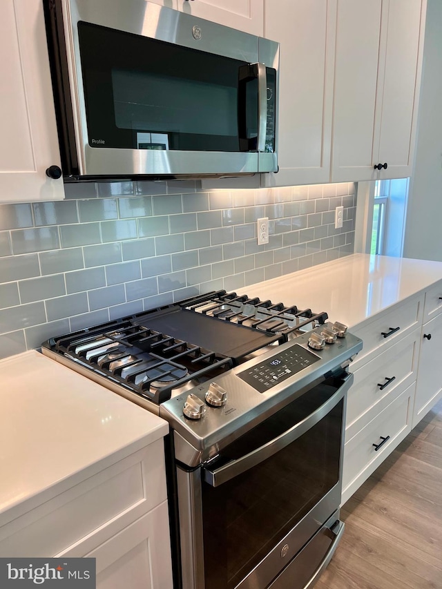 kitchen with light wood-type flooring, backsplash, white cabinetry, and stainless steel appliances