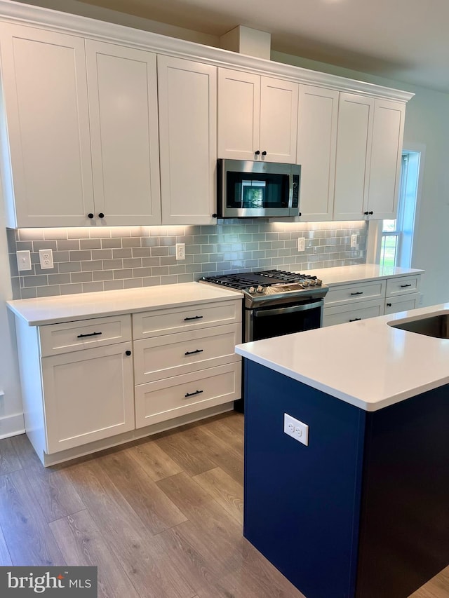 kitchen featuring a kitchen island, backsplash, white cabinetry, appliances with stainless steel finishes, and light hardwood / wood-style floors