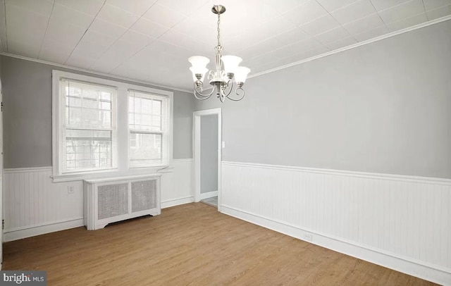 empty room with radiator heating unit, ornamental molding, light hardwood / wood-style flooring, and an inviting chandelier