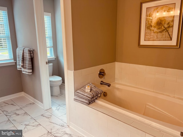 bathroom featuring plenty of natural light, tiled tub, toilet, and tile floors