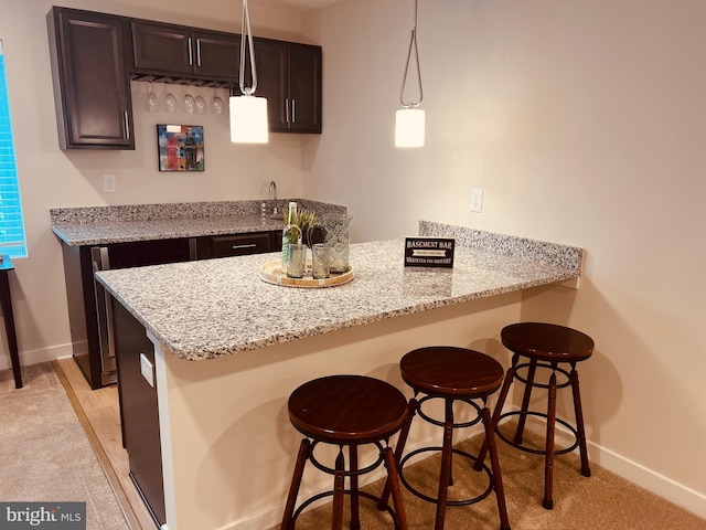 kitchen with kitchen peninsula, light stone counters, dark brown cabinets, decorative light fixtures, and a kitchen bar