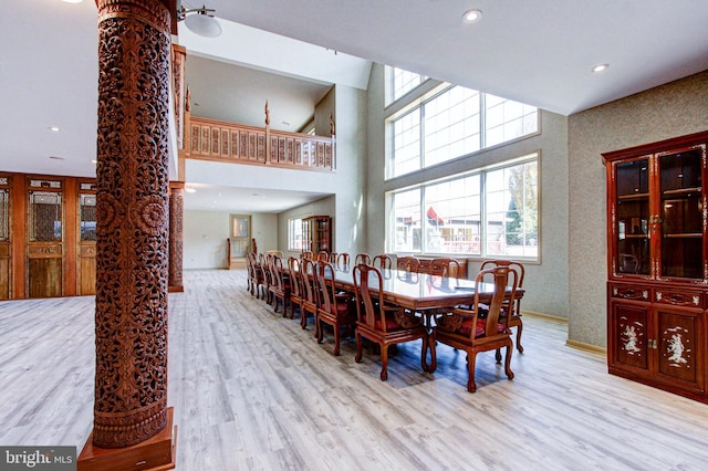 dining space with light hardwood / wood-style floors, decorative columns, and a towering ceiling