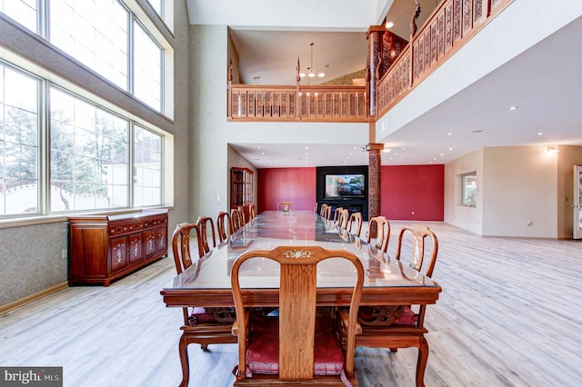 dining space featuring ornate columns, light hardwood / wood-style flooring, a fireplace, and a high ceiling