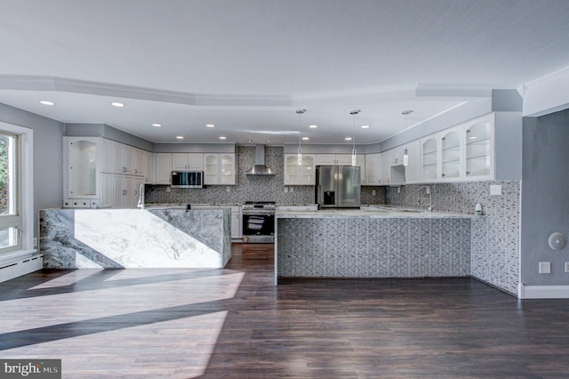 kitchen featuring pendant lighting, dark wood-type flooring, wall chimney exhaust hood, appliances with stainless steel finishes, and white cabinets