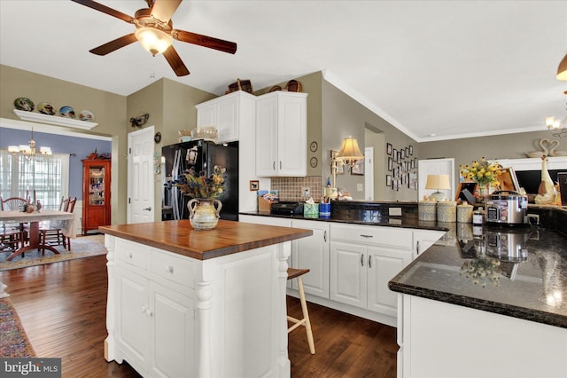 kitchen with black fridge, white cabinetry, hanging light fixtures, and ceiling fan with notable chandelier